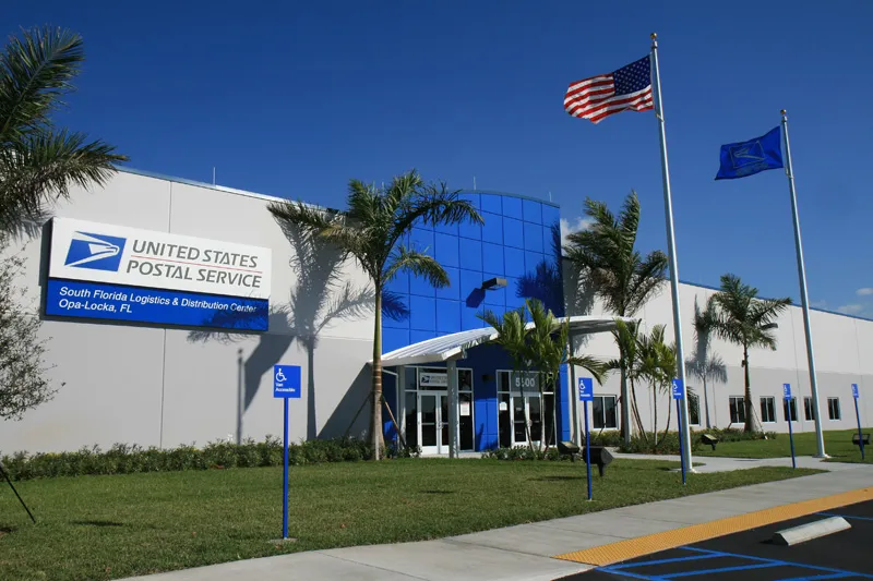 United States Postal Service South Florida Logistics and Distribution Center in Opa-Locka, FL with American and USPS flags flying outside.